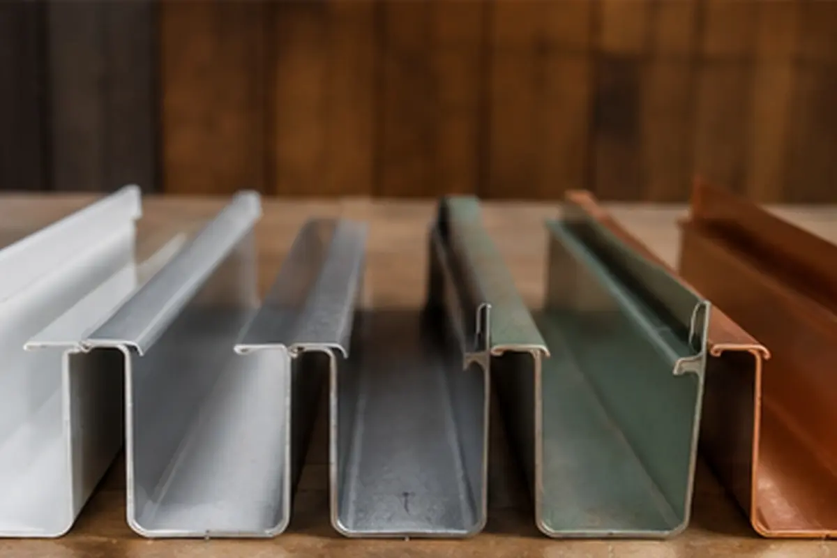 Gutter samples with different finishes arranged side by side on a wooden workbench.