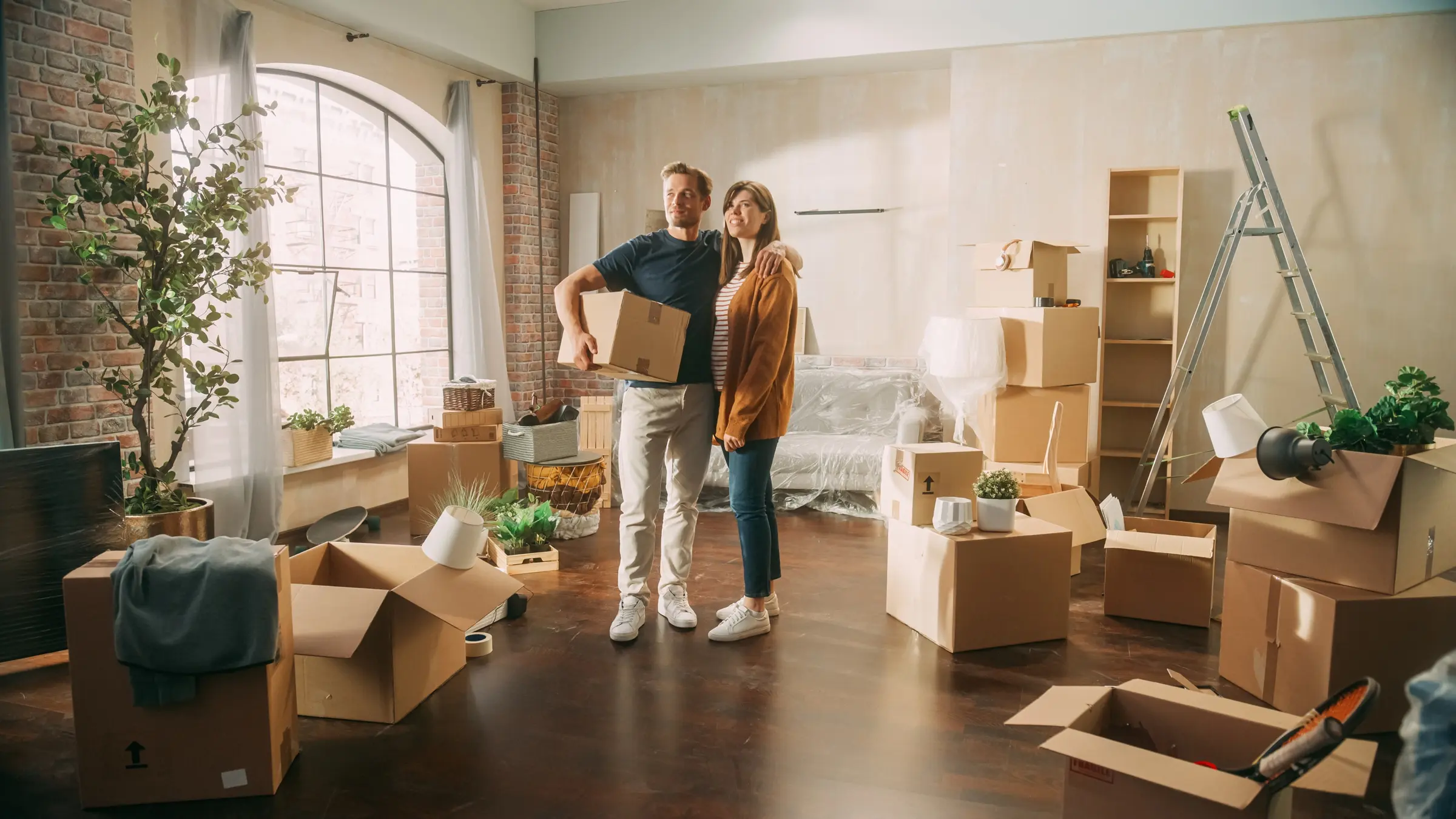 Couple standing in their living room surrounded by moving boxes and renovation supplies 