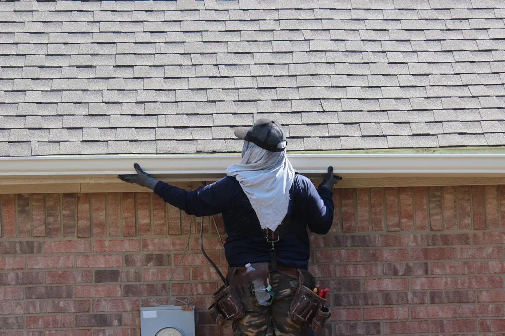 White gutter and downspout installed on a gray-sided residential gable