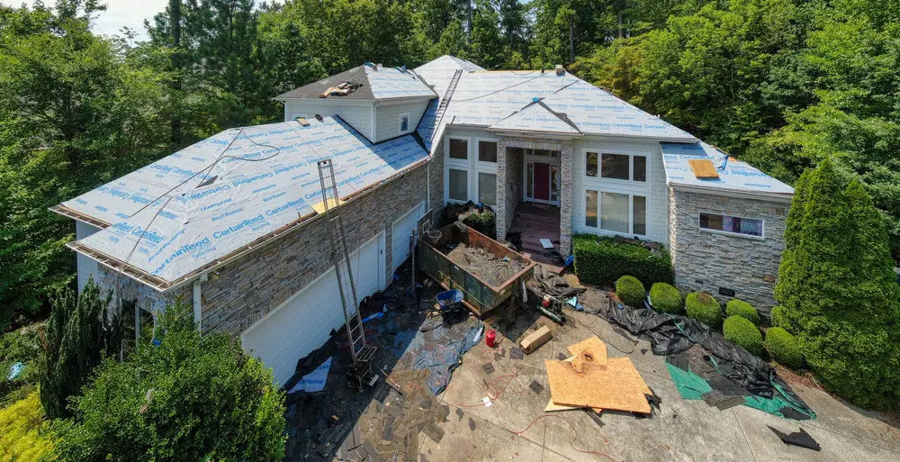 Residential roof replacement in progress with underlayment, dumpster, and property-protection tarps