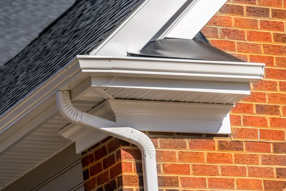 Vented soffit, fascia, gutter, and downspout at the corner of a brick house