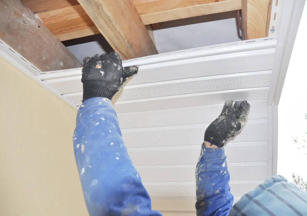 Contractor fitting white soffit panels beneath exposed roof framing